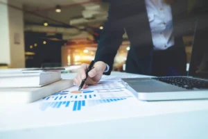 Professional person working in office pointing to printed graphs on desk.