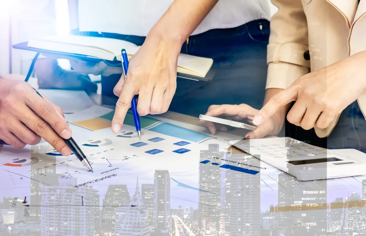 Hands of 3 colleagues pointing to data on printed paper on a desk in office.